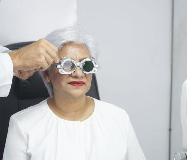 Woman sitting in optometrist cabinet having his eyesight checking, examining, testing with trial frame glasses by professional optician for new pairs of eyeglasses.