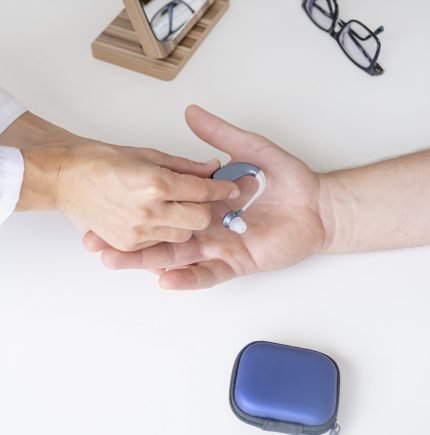 young male patient testing hearing aid in clinic exam room, young female doctor helping